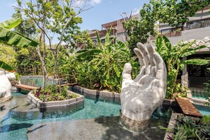 Ein Poolbereich mit einer großen, handgeformten Skulptur, umgeben von üppiger Bepflanzung und einem modernen Gebäude im Hintergrund.