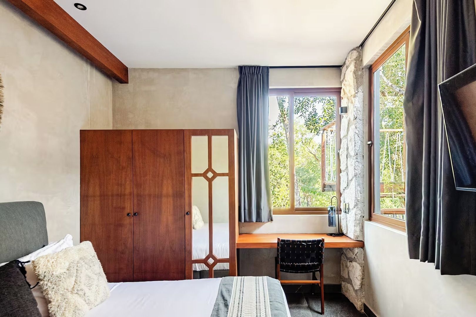 A bedroom with a bed, a desk, and a window with curtains.
