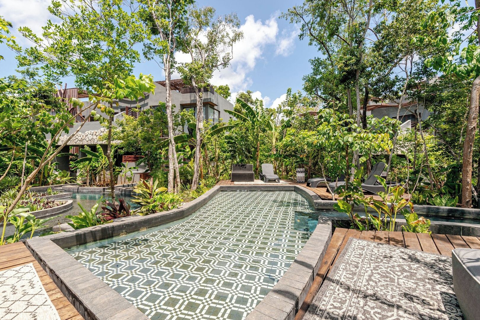 A pool area with a geometric tile pattern, surrounded by lush greenery and trees.