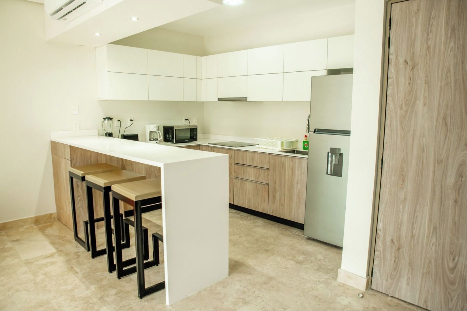 A modern kitchen with a central island, wooden cabinets, a microwave, and a refrigerator.