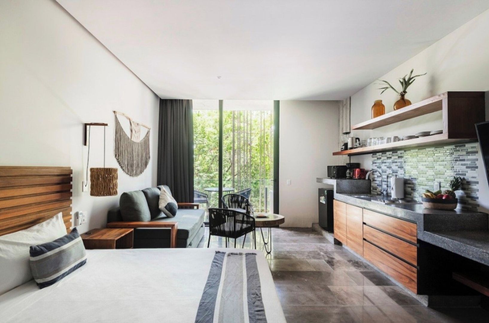 A modern hotel room with a bed, seating area, and kitchenette.