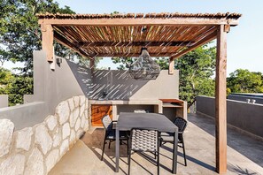 An outdoor patio with a pergola, a built-in grill, and a dining area with chairs and a table. - Selva Tulum · Private pool and rooftop · 1BR (Tulum)