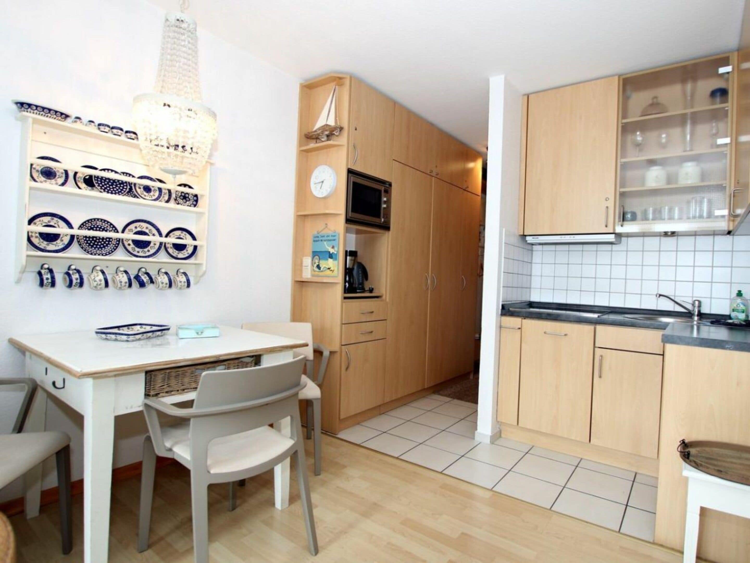 A compact kitchen with wooden cabinets, a microwave, and a sink. There is a dining table with chairs and a chandelier.