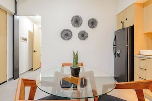 A modern kitchen with a glass dining table, wooden chairs, a refrigerator, and decorative wall art. - Rooftop Pool 2BR · 2 min to 5th Ave and Beach (Playa del Carmen)