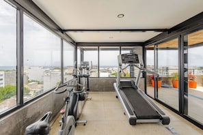 A balcony with a treadmill and stationary bikes, large windows, and potted plants. - Rooftop Pool 2BR · 2 min to 5th Ave and Beach (Playa del Carmen)