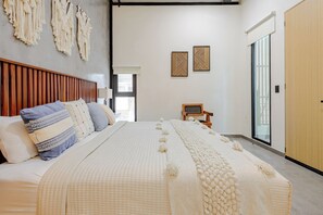 A bedroom with a bed, pillows, a chair, a wall with artwork, and a sliding door. - Rooftop Pool 2BR · 2 min to 5th Ave and Beach (Playa del Carmen)
