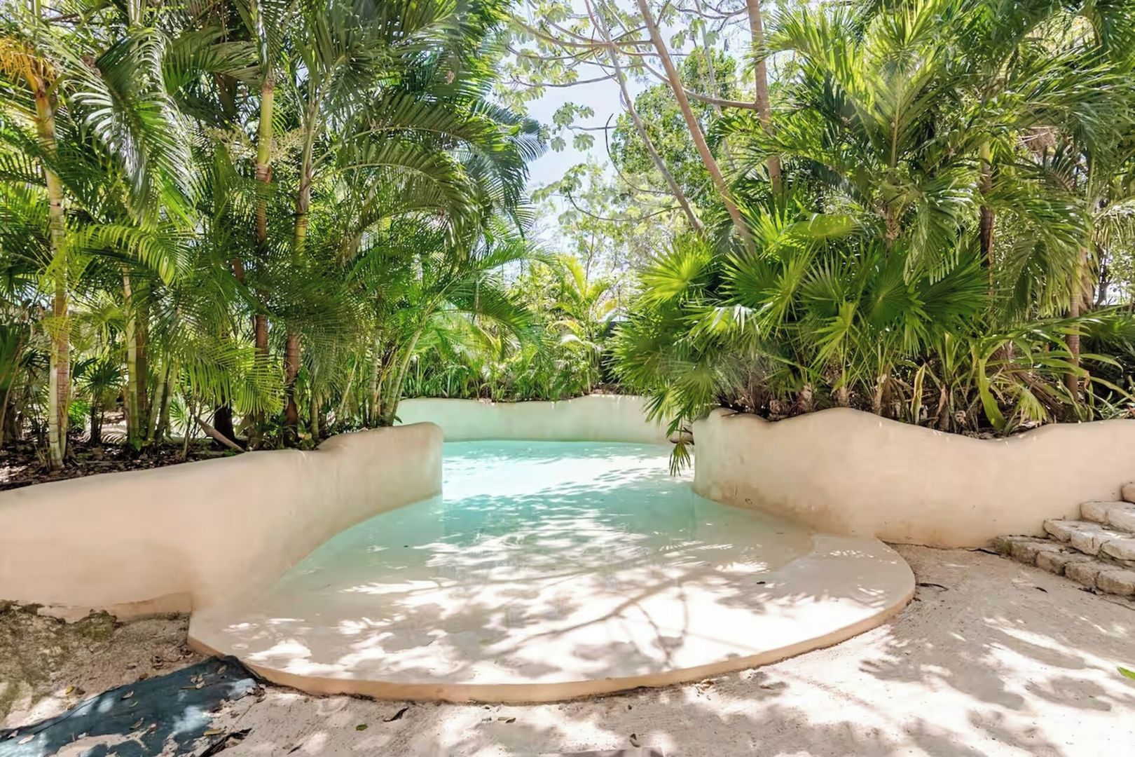 A circular pool with a sandy edge, surrounded by lush green foliage.