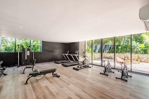 A modern gym with exercise equipment, large windows, and a view of greenery. - Premium studio · Private immersion · Gym and Sauna (Tulum)