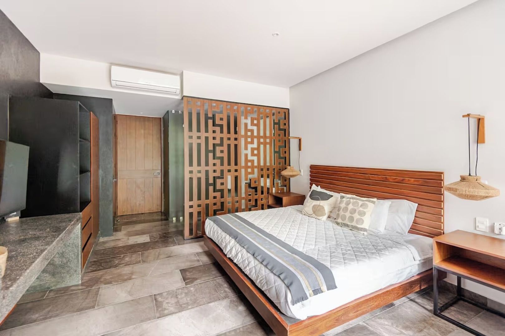 A modern bedroom with a wooden bed, a nightstand, a decorative screen, and a built-in wardrobe.
