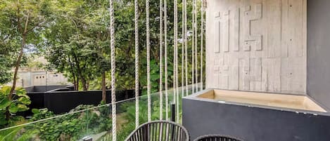 An outdoor seating area with a table and chairs, surrounded by greenery and a rope swing.