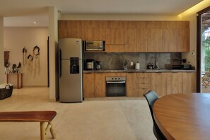A modern kitchen with wooden cabinets, stainless steel appliances, and a dining area with a round table. - 3BR Favorite · Private Pool + Cenote · Tulum (Tulum)