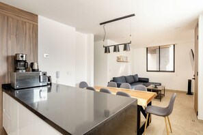A modern kitchen with a central island, a dining area with a wooden table and chairs, and a living space with a sofa and a coffee machine. - 3BR Favorite · Private Pool + Cenote · Tulum (Tulum)