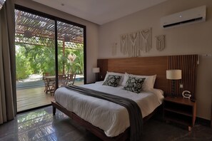 A bedroom with a large bed, a wooden headboard, two bedside lamps, and a view of a patio with a table and chairs. - 3BR Favorite · Private Pool + Cenote · Tulum (Tulum)