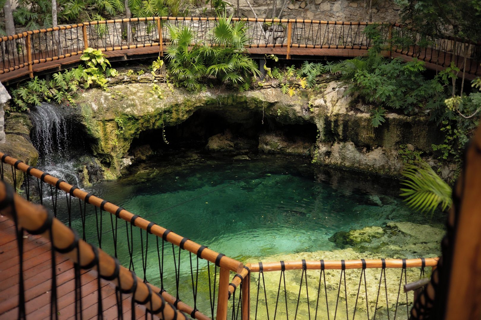 A clear pool with a wooden deck and a stone bridge.