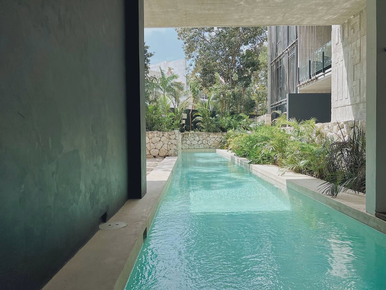 A swimming pool with a stone wall and greenery on one side.