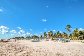 A beach with palm trees, beach umbrellas, and a few people. - Main Street to the beach | Coba Av. (Tulum)
