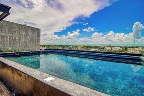 A rooftop swimming pool with clear blue water, surrounded by a concrete wall and a view of the cityscape. - Main Street to the beach | Coba Av. (Tulum)