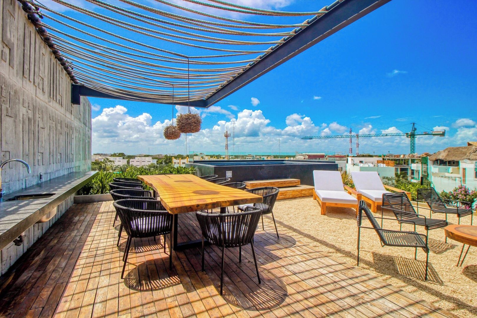 A rooftop terrace with a wooden table, black chairs, and lounge chairs under a striped canopy.