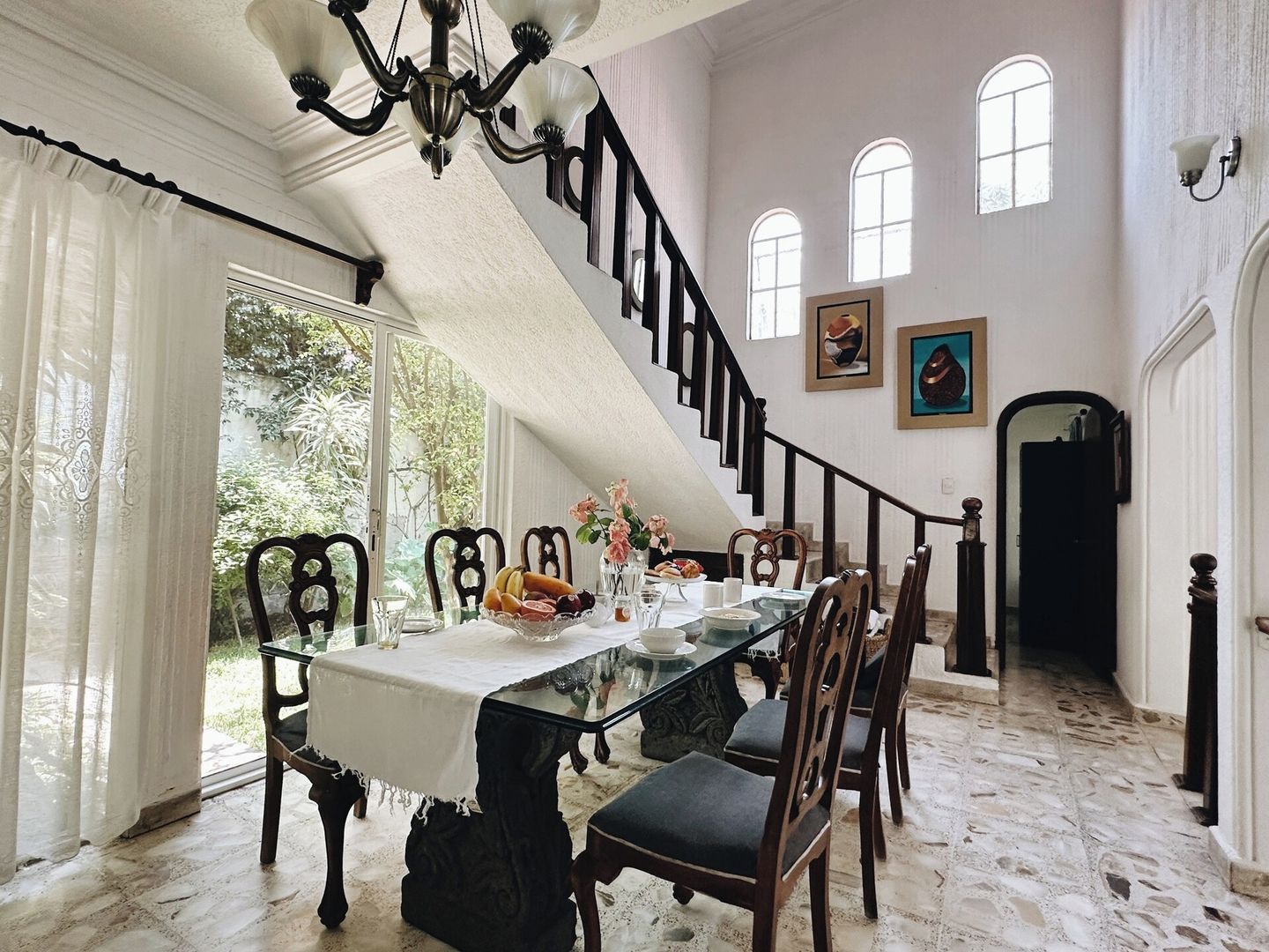 A dining area with a glass table, chairs, and a staircase leading to an upper level.