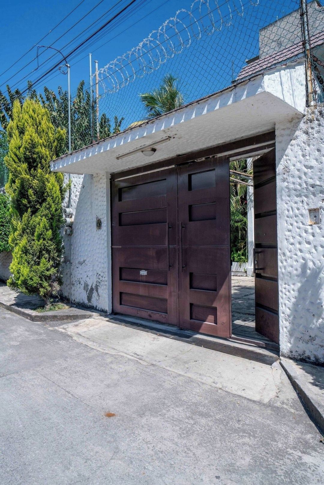 Un garaje con puerta marrón, pared blanca y cerca de seguridad con alambre de púas.