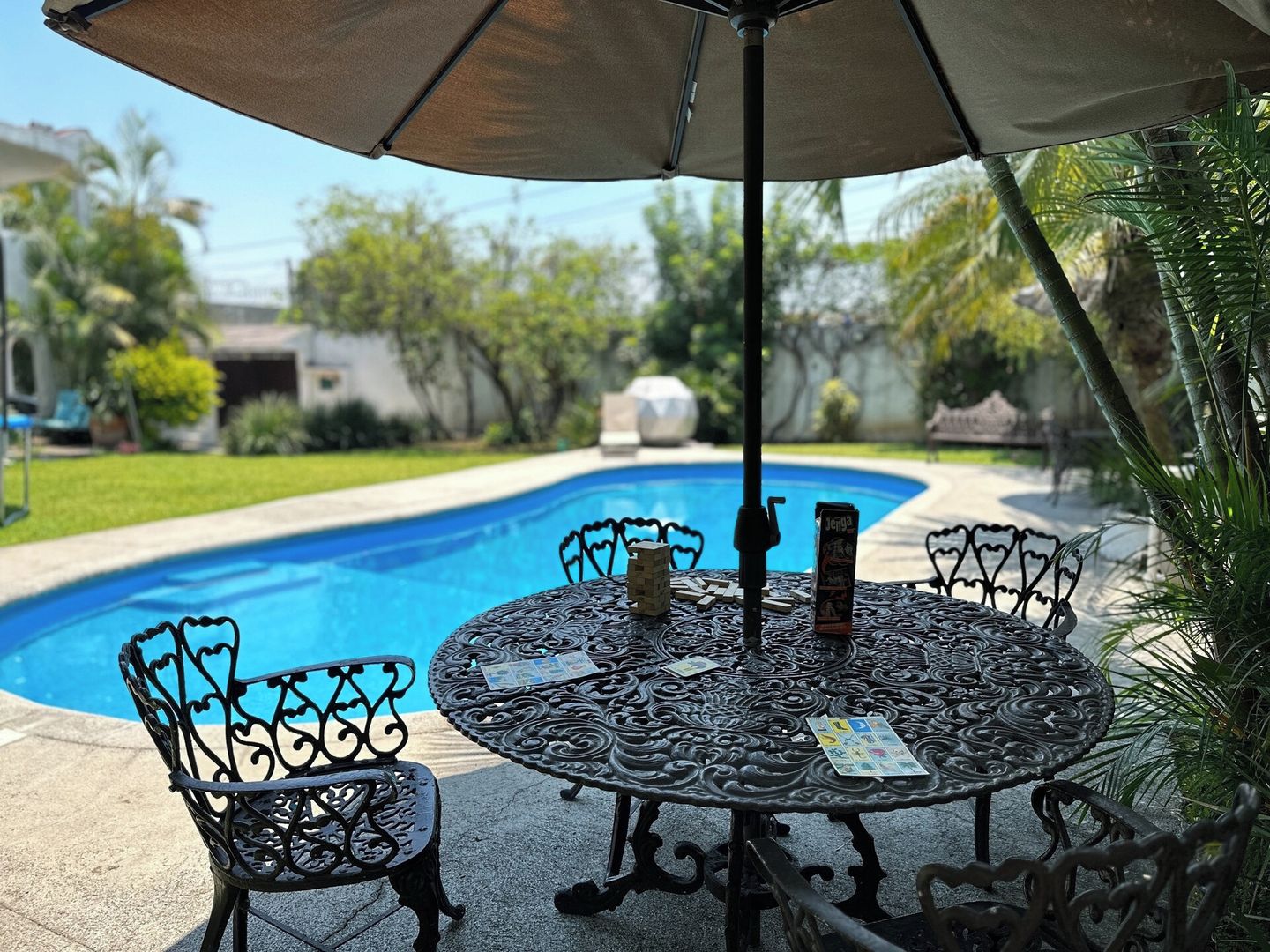 Ein Poolbereich mit runden Tisch und Stühlen, einem Sonnenschirm und einem Pool.
