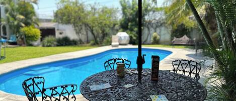 Ein Poolbereich mit runden Tisch und Stühlen, einem Sonnenschirm und einem Pool.