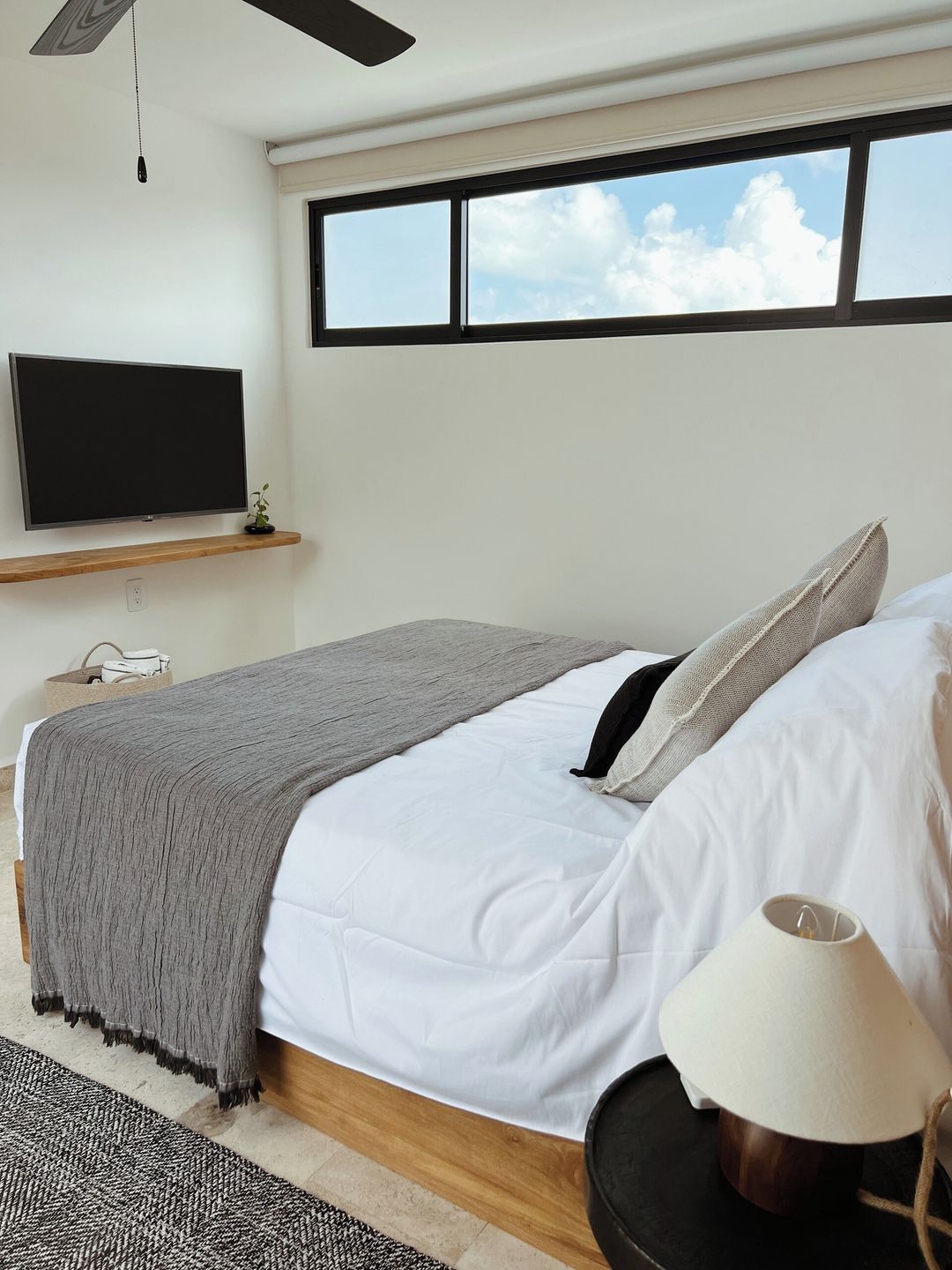 Une chambre à coucher avec un lit, une lampe de chevet, un téléviseur fixé au mur et une fenêtre donnant sur le ciel.