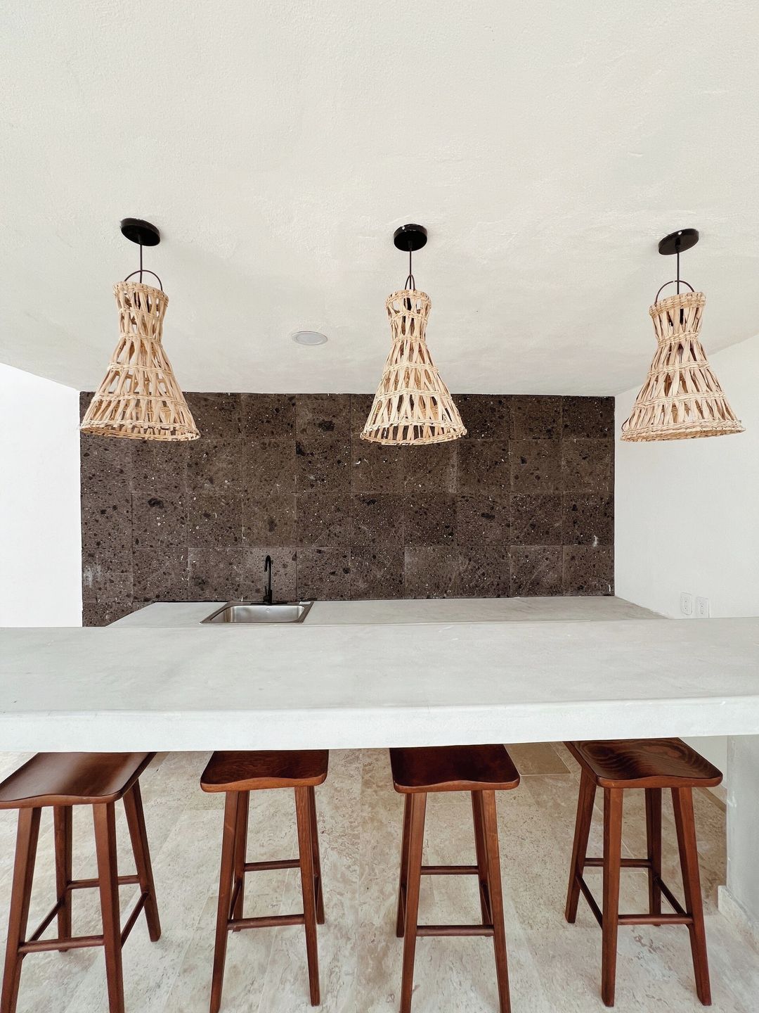 A kitchen with a white countertop, three wooden stools, and three woven pendant lights.