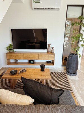 Ein modernes Wohnzimmer mit Flachbildfernseher, Holzmöbeln, einem Couchtisch und einer großen Topfpflanze.