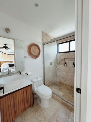 A modern bathroom with a large mirror, a vanity with a sink, a toilet, and a glass-enclosed shower area. - PH con alberca privada (Tulum)