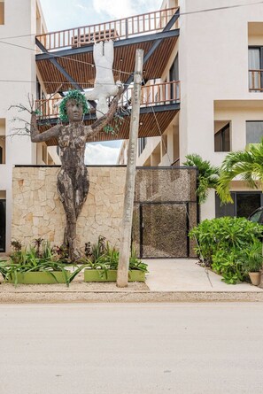 A statue of a woman with outstretched arms in front of a building with balconies and a stone wall. - Stylish Tulum Apt w/Jacuzzi and Pools (Tulum)