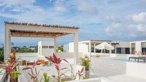 Ein moderner Poolbereich im Freien mit einer Pergola, Liegestühlen und einem weißen Sonnenschirm.