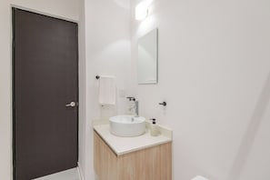 Un baño con una puerta oscura, un lavabo blanco, un espejo y una toalla colgada en la pared.