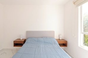 A bedroom with a bed, two bedside tables, and a window.