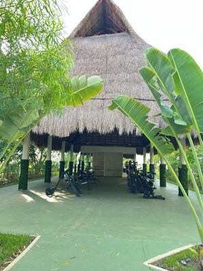 Een gebouw met rieten dak en fitnessapparatuur ervoor.