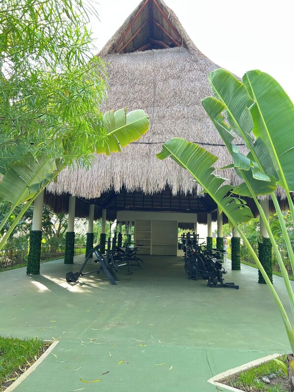 A thatched-roof structure with exercise equipment in front.