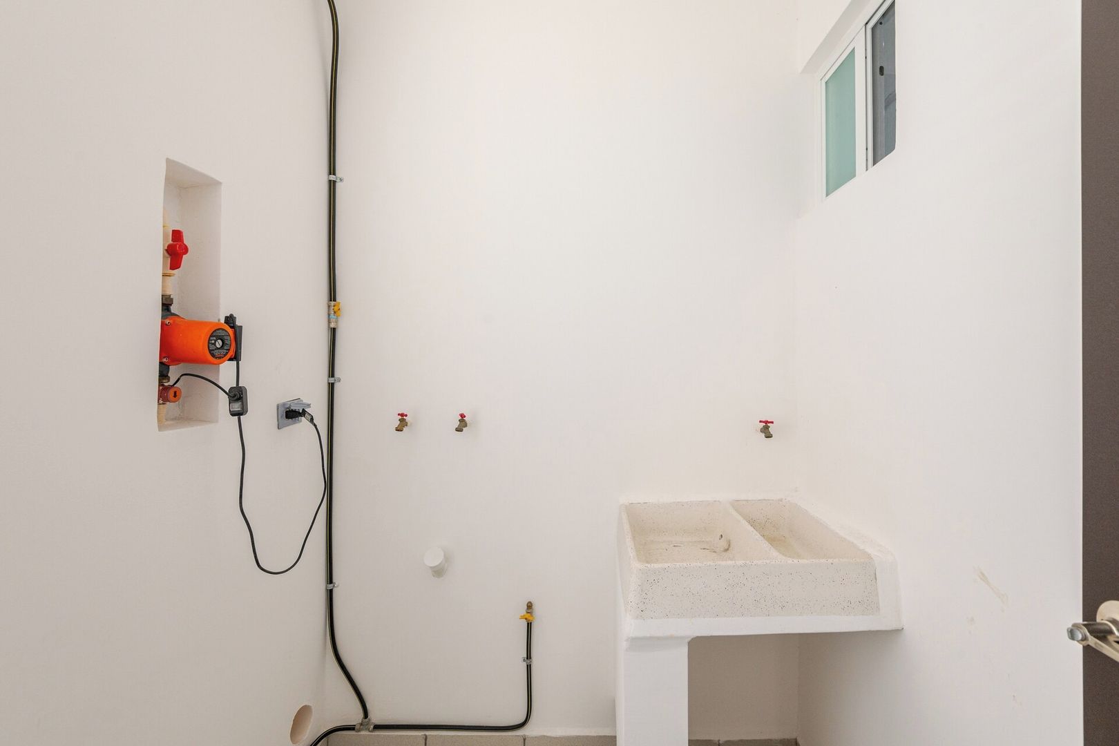 Ein Badezimmer mit einem weißen Waschbecken, einem roten Warmwasserbereiter und freiliegenden Rohren.