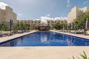 Una piscina con sillas de descanso y sombrillas, rodeada de edificios con balcones.