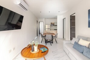 Een moderne woonkamer met een grijze bank, een houten salontafel en een aan de muur bevestigde televisie.