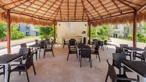 Eine Terrasse im Freien mit einem Reetdach, ausgestattet mit Tischen und Stühlen sowie einem Grillbereich.