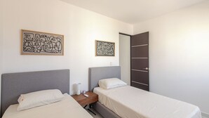 Ein Doppelzimmer mit zwei Betten, einem Nachttisch mit Lampe und zwei abstrakten Wandbildern.