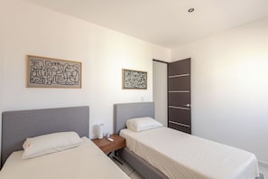 Habitación doble con dos camas, una mesita de noche con lámpara y dos obras de arte abstractas en la pared.