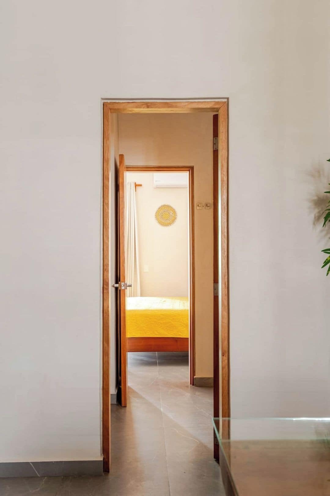 A hallway leading to a room with a bed, a circular wall decoration, and a plant.