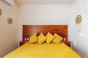 A room with a wooden headboard, a yellow bedspread, and a wall-mounted macrame decoration. - Modern Apartment with Jacuzzi (Tulum)