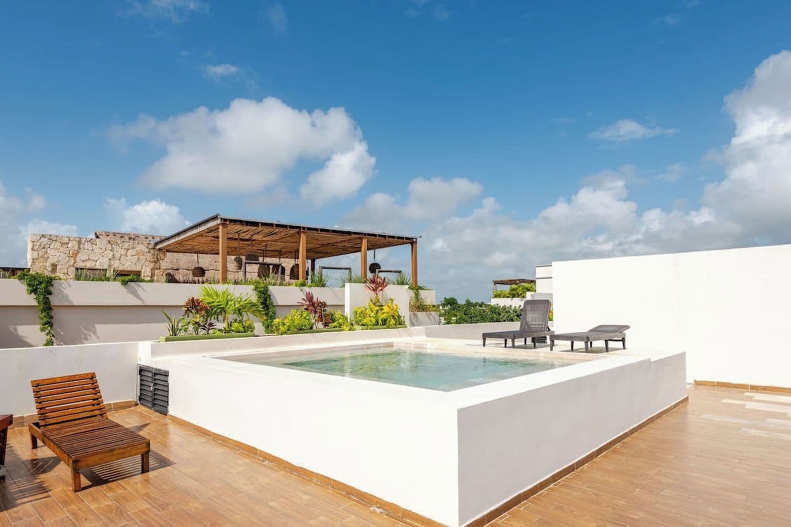 A rooftop pool area with a pergola, lounge chairs, and a stone building in the background.