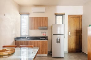 A compact kitchen with a refrigerator, a sink, wooden cabinets, and a window. - Modern Apartment with Jacuzzi (Tulum)