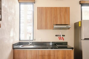 Eine Küche mit Spüle, Holzschränken, einem Edelstahlkühlschrank und einem Fenster mit Jalousien.