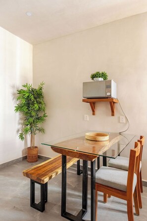 Ein moderner Essbereich mit einem Glastisch, Holzstühlen, einer Bank, einem Blumentopf und einem Fernseher auf einem Holzregal.