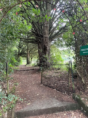 A pathway leading into a wooded area with a metal gate and a directional sign. - Charming 1-bedroom cottage on 33 acre woodland estate with hot tub & log burner (Hollybush)