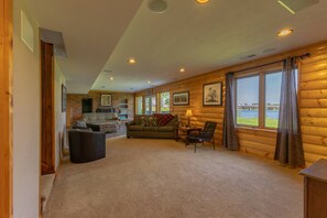 Ein Holzhäuschen-Interieur mit Kamin, einer Couch, einem Couchtisch und Blick auf ein Gewässer durch große Fenster.